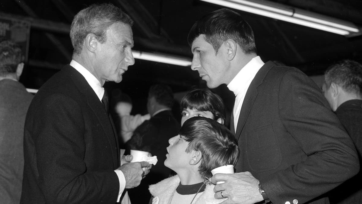 Adam Nimoy standing in front of his father looking up at a man.