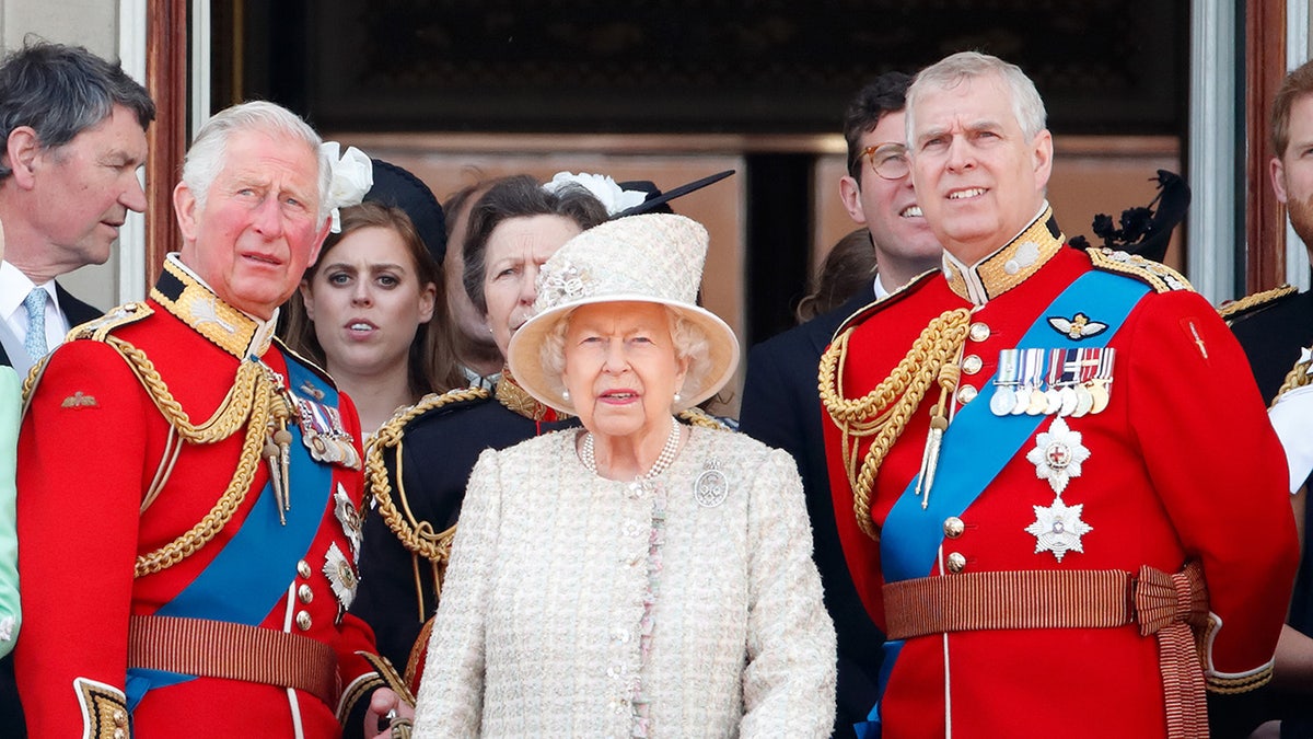 Queen Elizabeth II standing on the palace balcony in between Prince Charles and Prince Andrew in uniform.