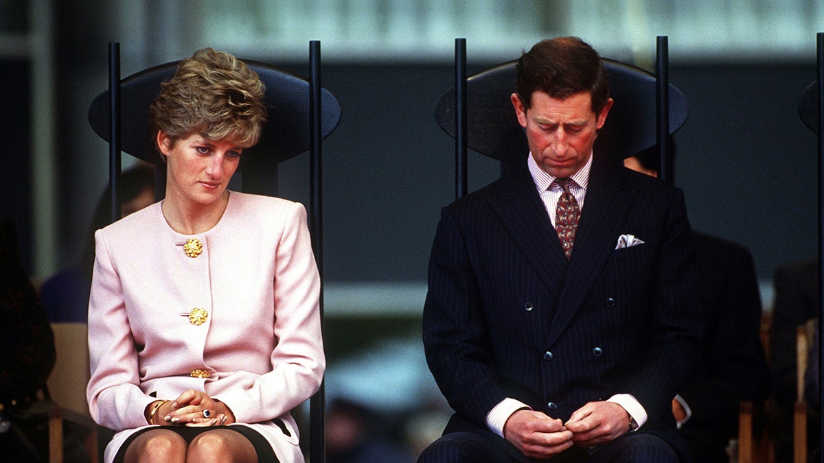 Princess Diana wearing a pink blazer sitting next to Prince Charles in a dark suit and maroon tie.