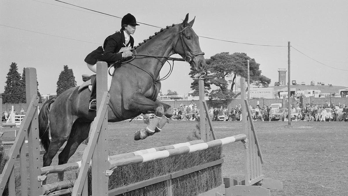 Princess Annes horse jumps over a fence in a black and white photo.