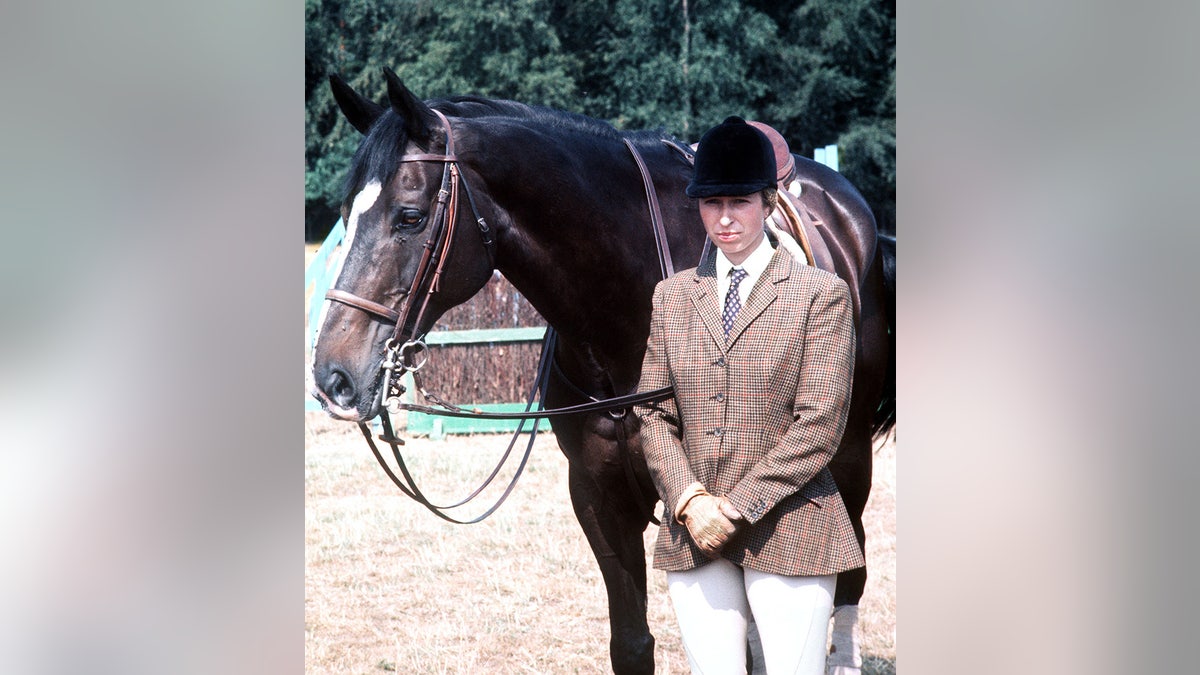 Princess Anne posing next to her horse in equestrian gear.