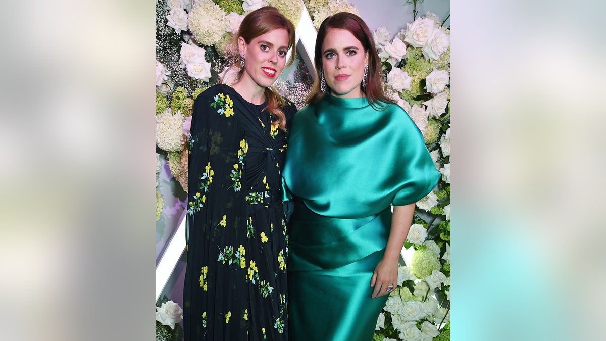 Princess Beatrice in a black and yellow floral dress standing next to Princess Eugenie in a green satin dress.