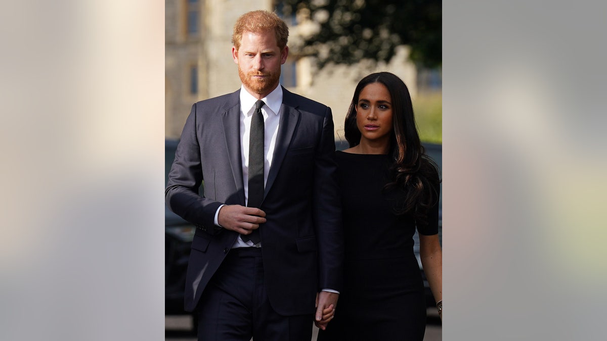 Meghan Markle wearing a black dress next to Prince Harry in a dark suit and skinny black tie.
