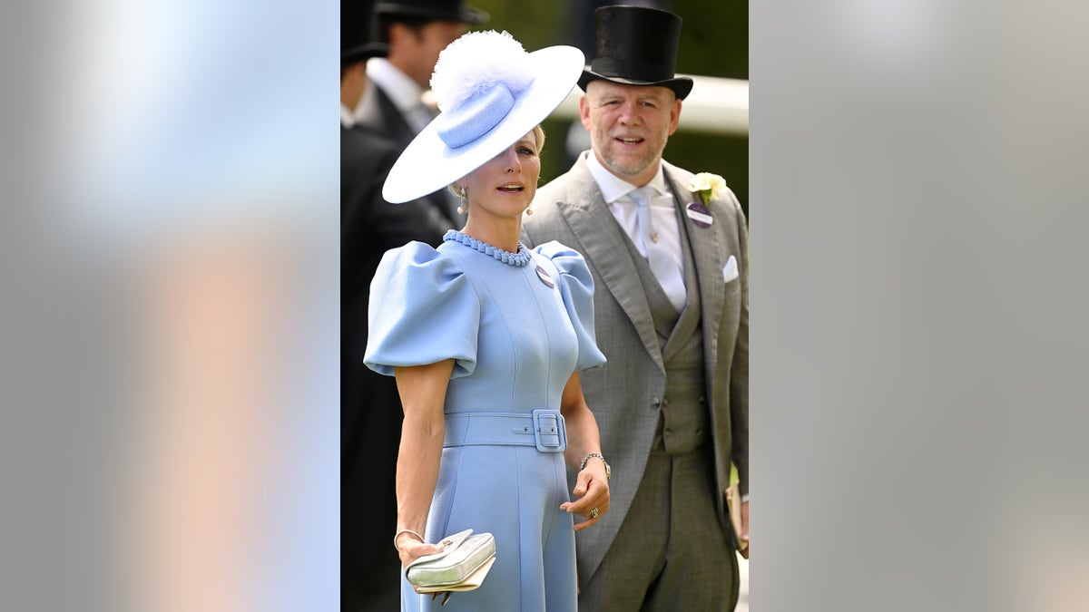 Zara Tindall wearing a light blue dress and a matching hat standing next to Mike Tindall in a grey suit and a black top hat.