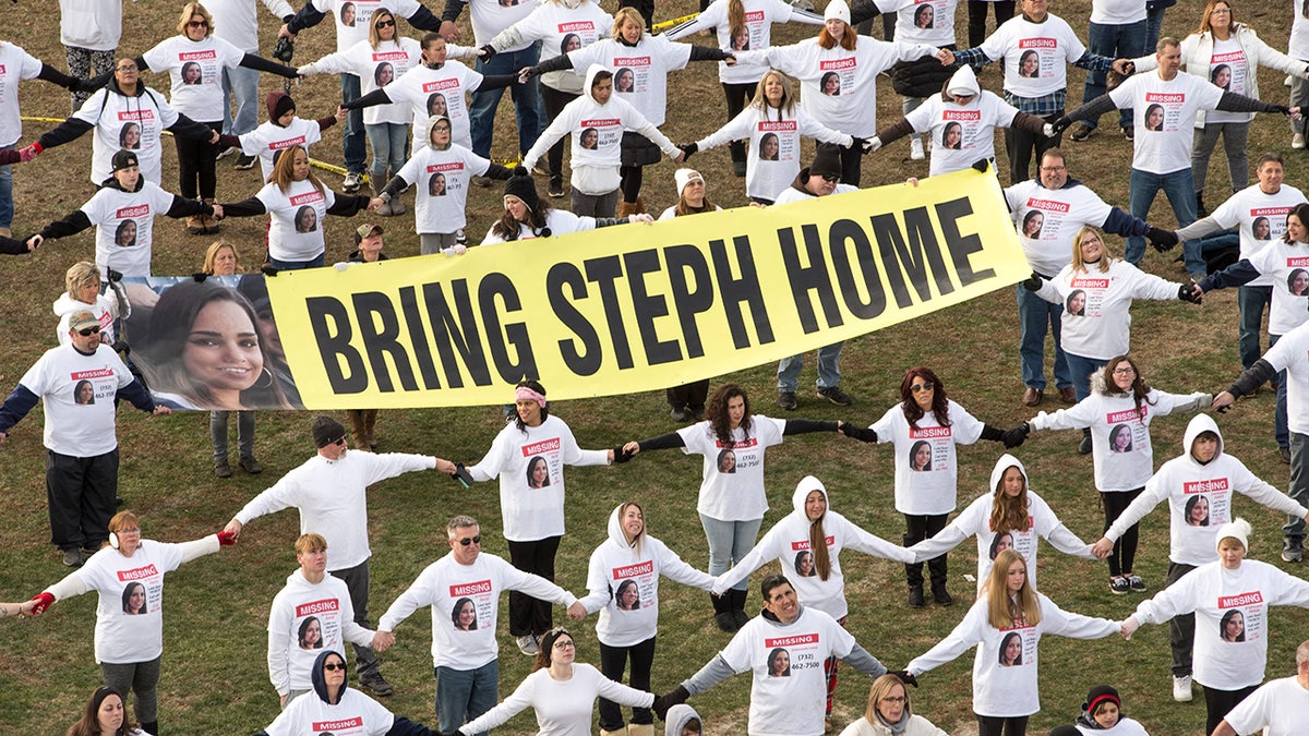 Volunteers hold hands with banners that read take Steph home