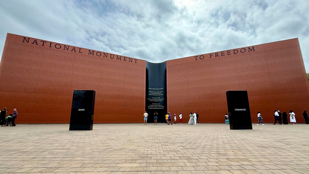 The towering brown stone National Monument to Freedom stands in a great pavilion in Freedom Monument Sculpture Park in Montgomery, Alabama. Two black stones inscribed with the words "hope" and "strength" stand before it.