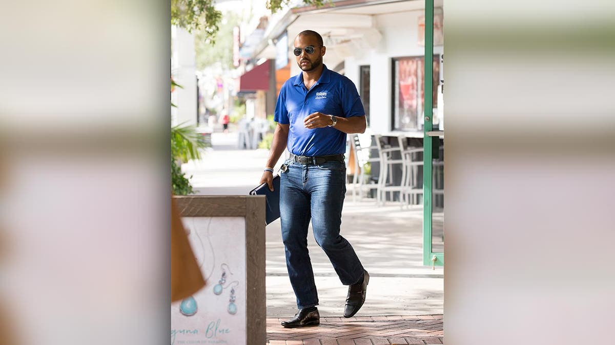 A man in jeans and a polo shirt walks along a paved sidewalk