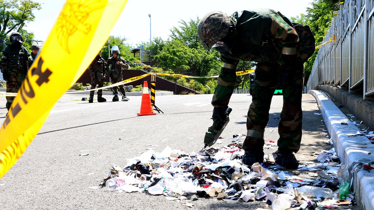 A South Korean soldier wearing protective gear inspects debris from a balloon, allegedly sent by North Korea, behind yellow crime scene tape.