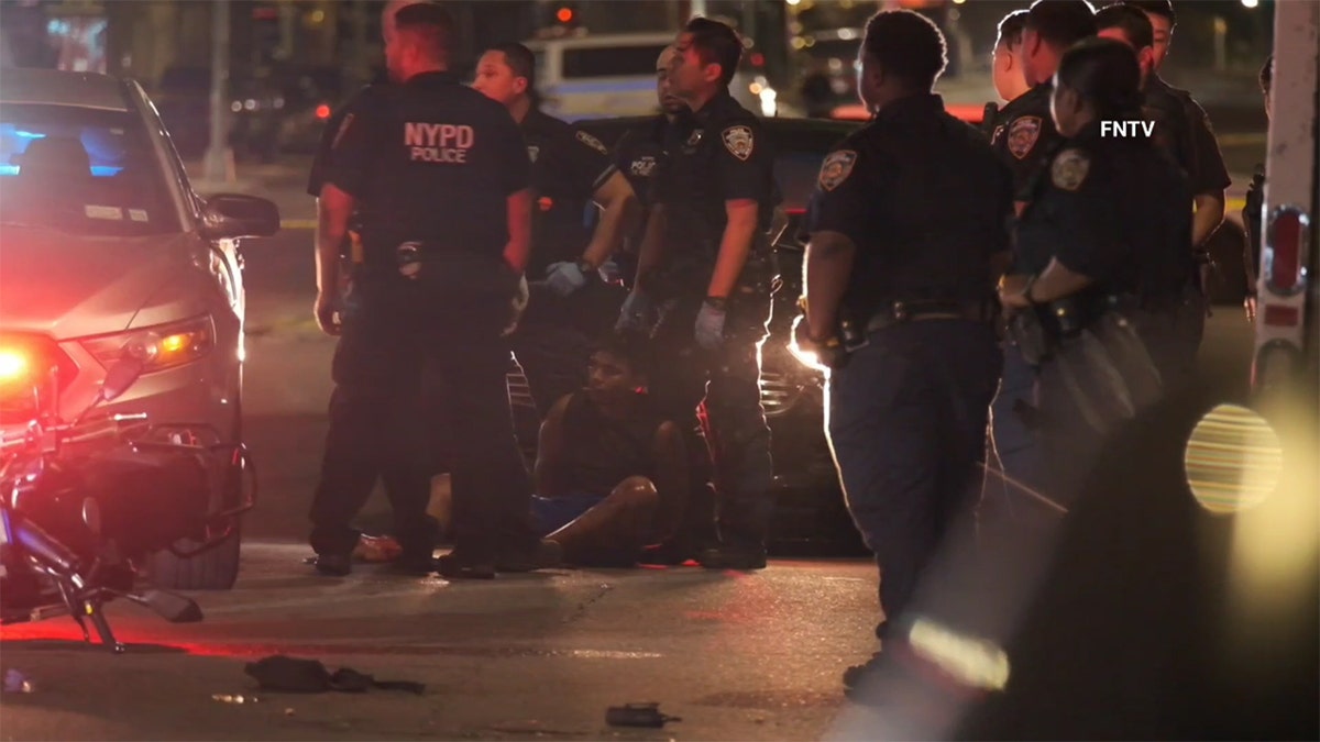 The suspect is arrested, sitting on the floor and surrounded by NYPD.