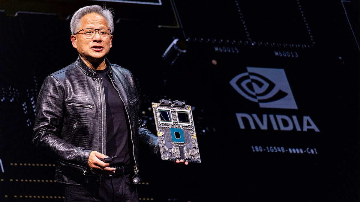 Huang holding a circuit board while giving a speech.