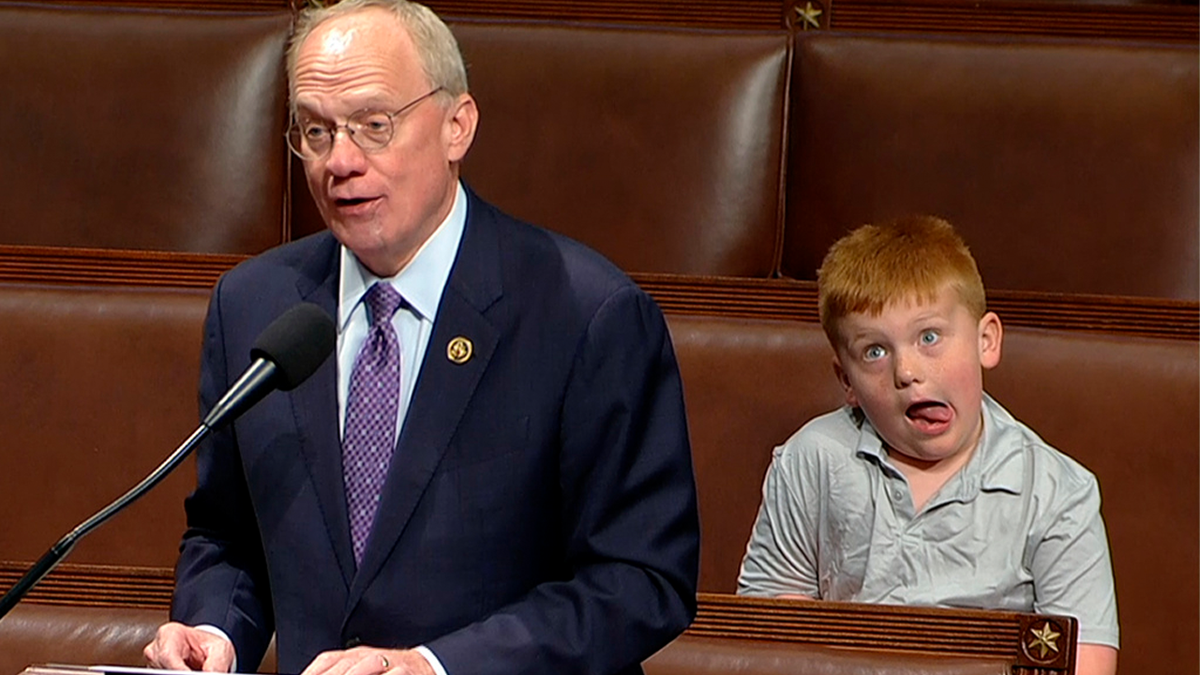 Rep John Rose gives speech on House floor, with his son visible behind him