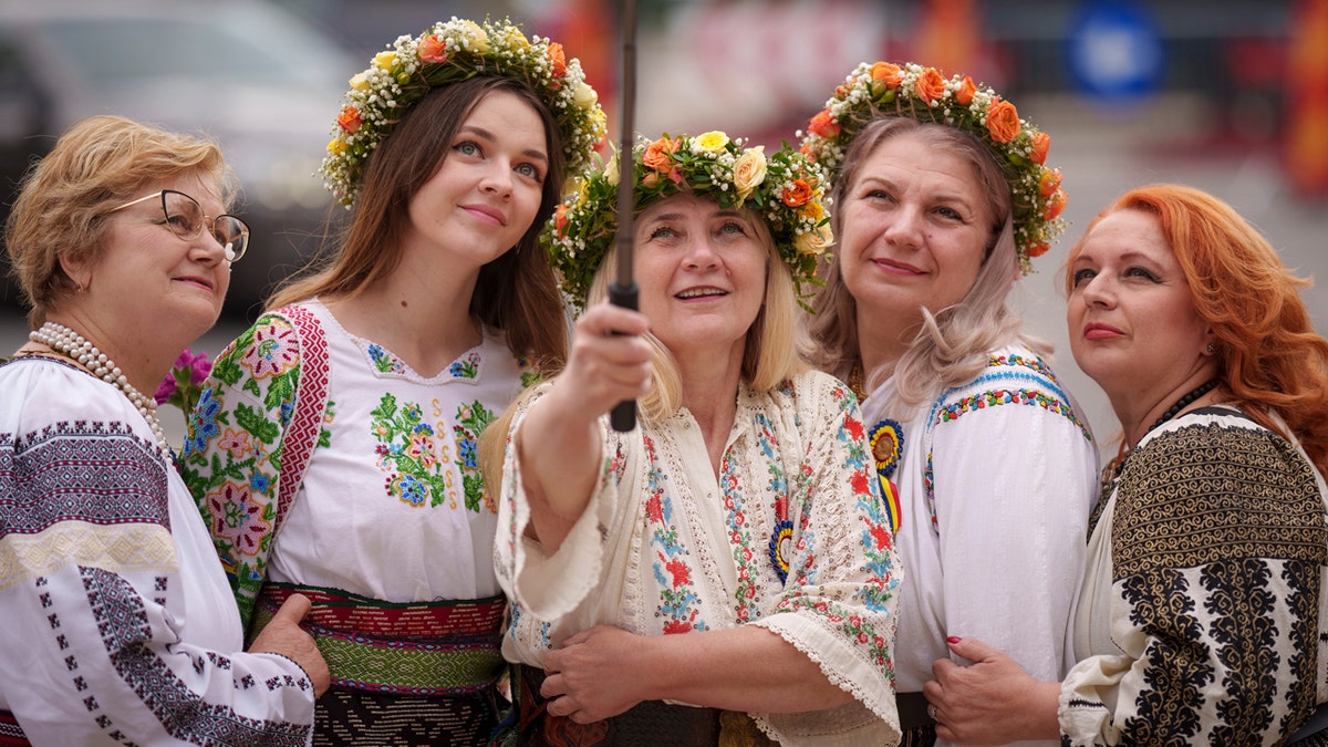 Women wearing Romanian traditional blouses, known in Romanian as an "IE" pose for a selfie photograph.