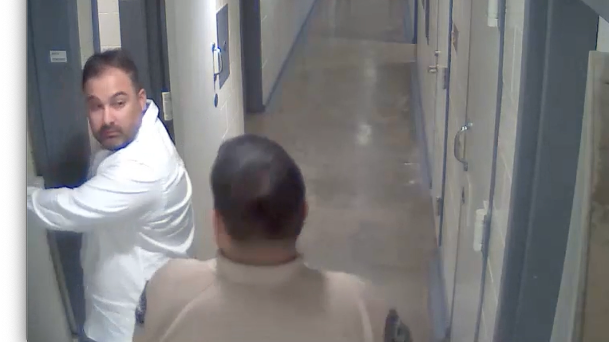 Joseph Iniguez olha por cima do ombro para um policial ao entrar em uma cela