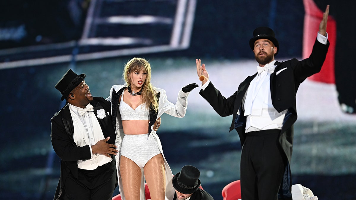 Travis Kelce inn a top hat and tuxedo performs with Taylor Swift in a two piece outfit