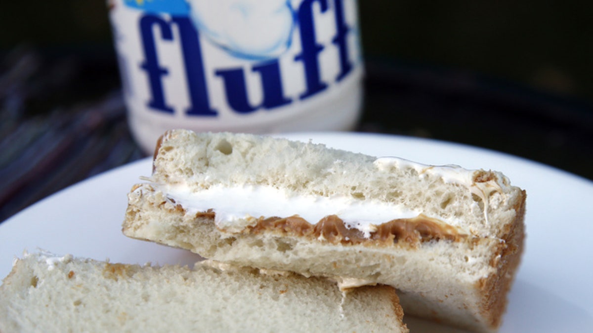 Um sanduíche Fluffernutter é mostrado em um prato enquanto um pote de Marshmallow Fluff é visível ao fundo.