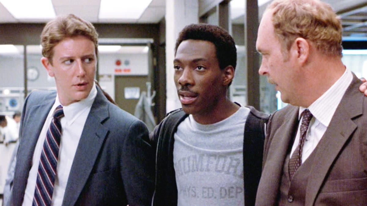 O juiz Reinhold de terno, Eddie Murphy de camiseta cinza e moletom preto e John Ashton de terno bege "Policial de Beverly Hills"