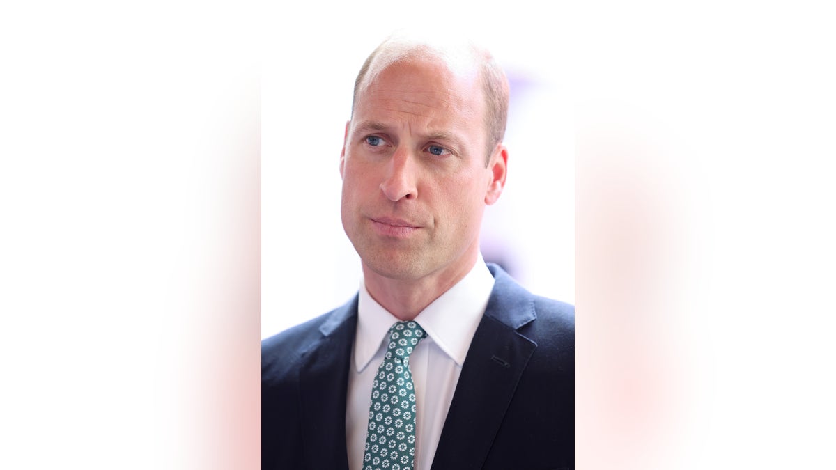 A close-up of Prince William looking serious in a navy blazer and a green printed tie.