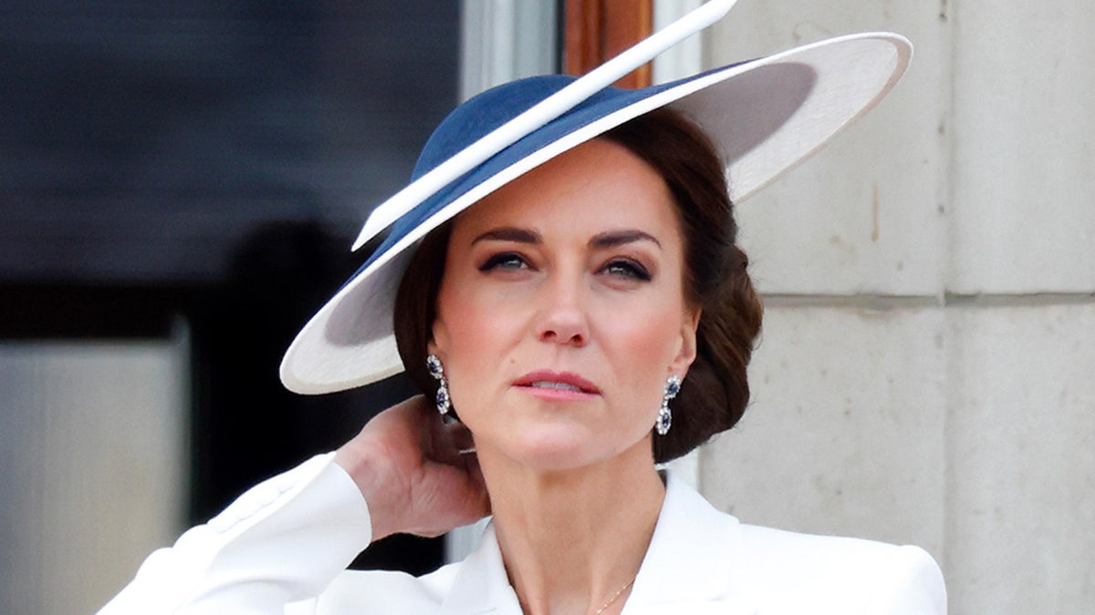 A close-up of Kate Middleton wearing a striped blue and white hat with a matching white dress