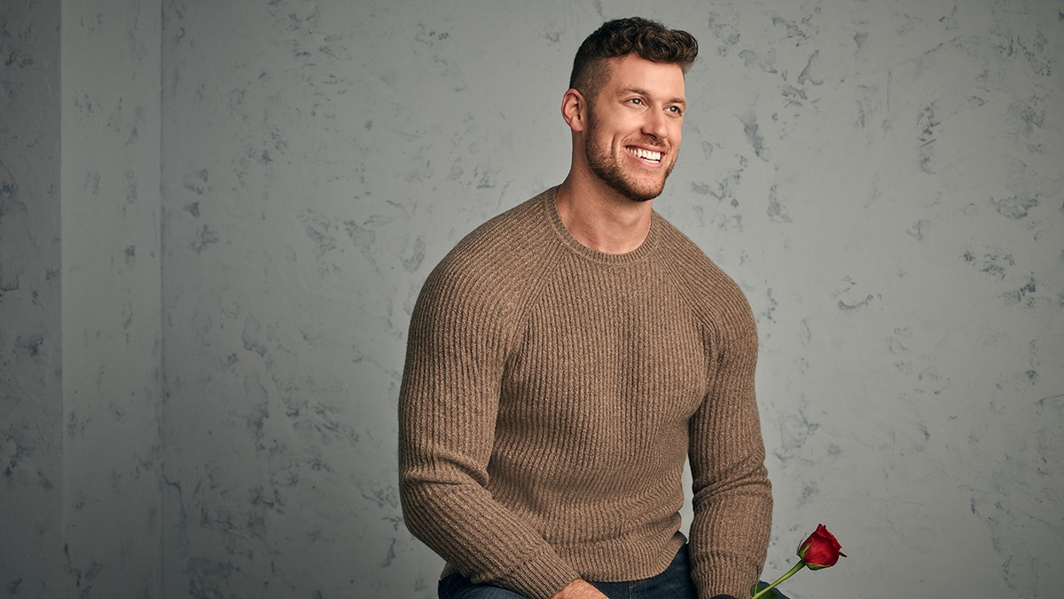 Bachelor contestant Clayton Echard holds a rose while wearing brown sweater