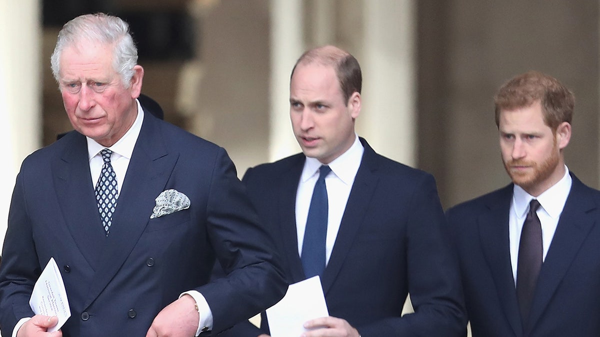 King Charles walking in front of Prince William and Prince Harry as they wear matching navy suits.