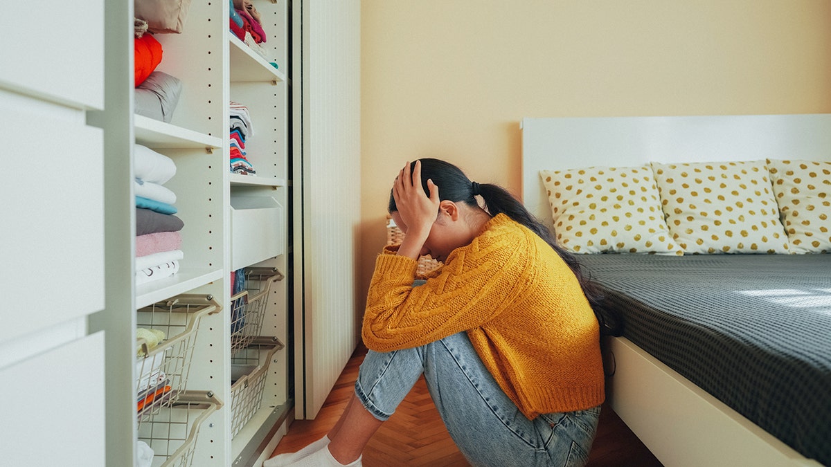 Girl with her head in her hands sitting on the floor beside her bed