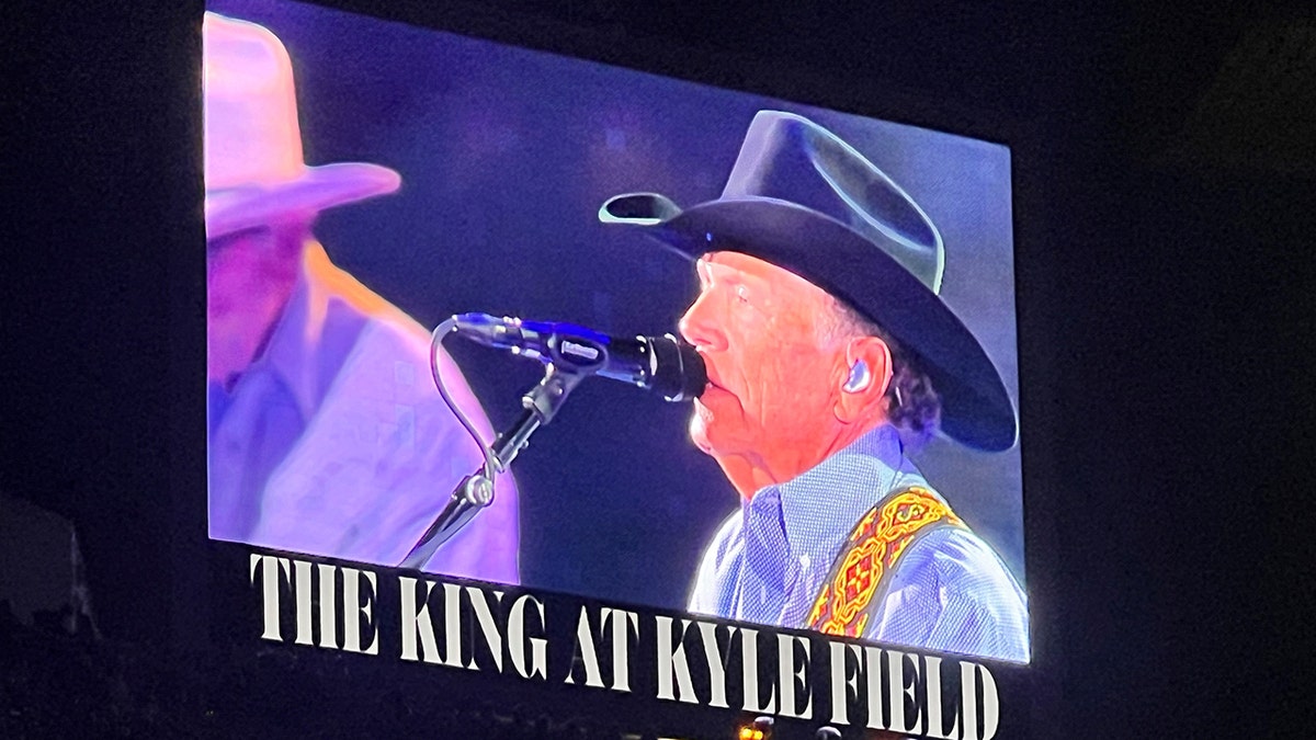 George Strait wears black cowboy hat while singing into a microphone