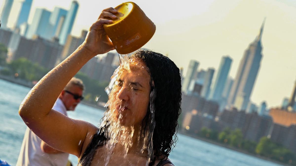 A woman pours water on her face to cool off in a fountain in Domino Park, Brooklyn with the Manhattan skyline in the background as the sun sets during a heat wave on July 24, 2022.