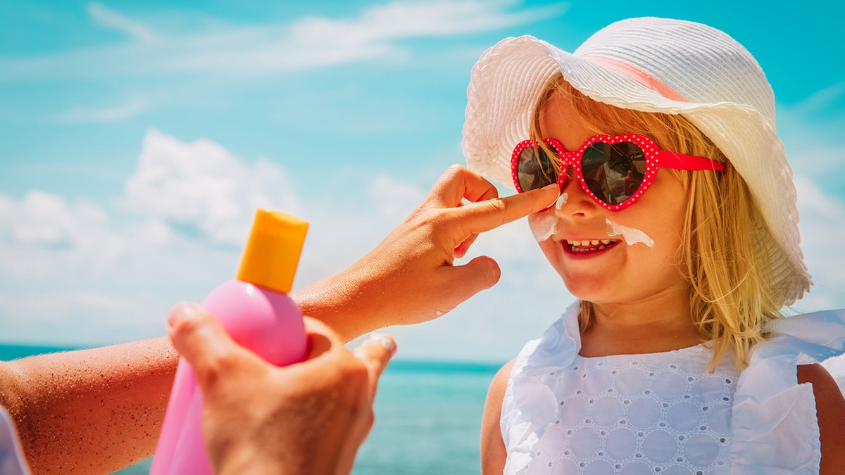 a little girl has sunscreen applied to her face