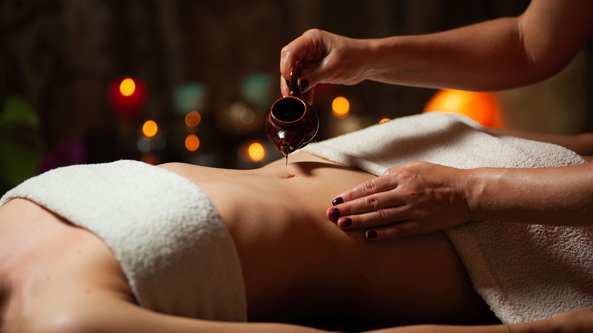 A woman has oil placed in her navel during a massage
