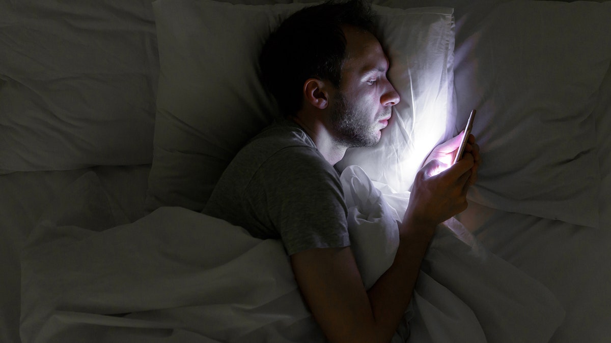 man on phone late at night lying in bed 