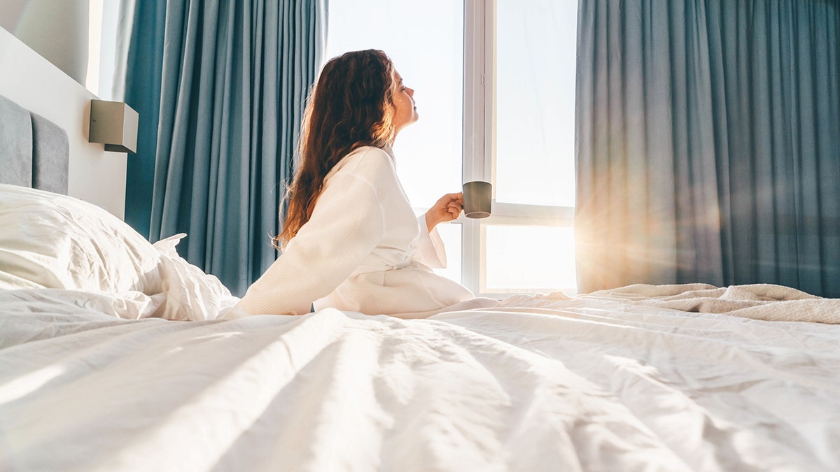 woman sits in bed with coffee early in the morning