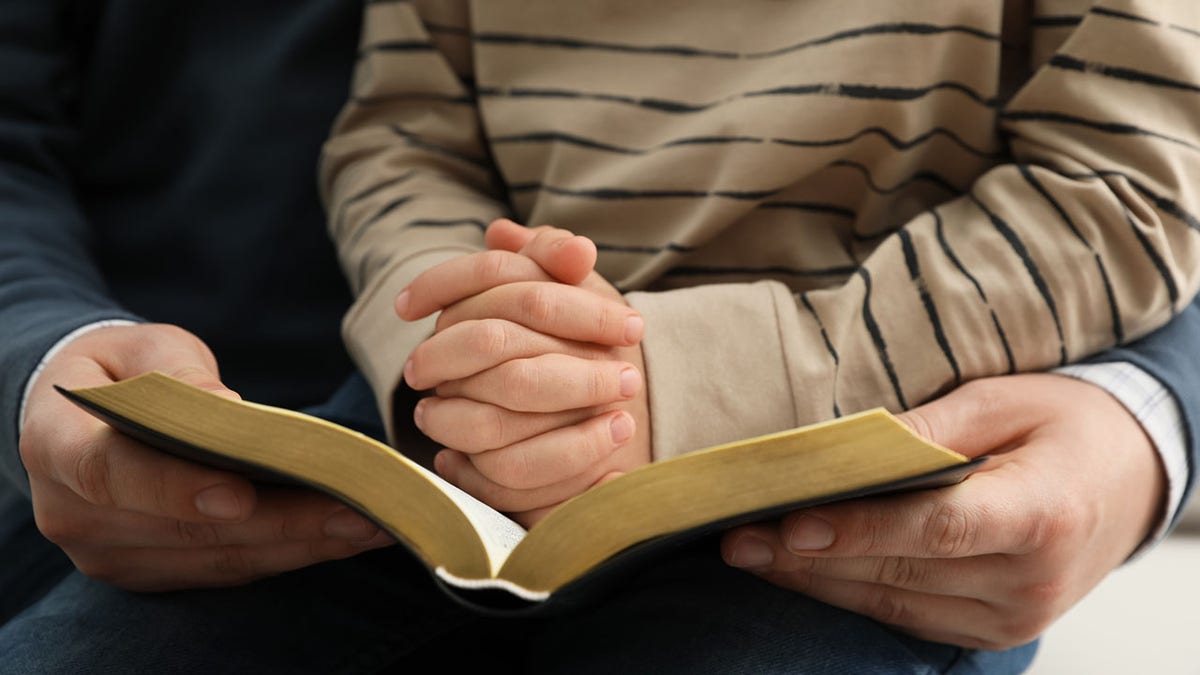 Anak laki-laki dan orang tuanya membaca Alkitab bersama,