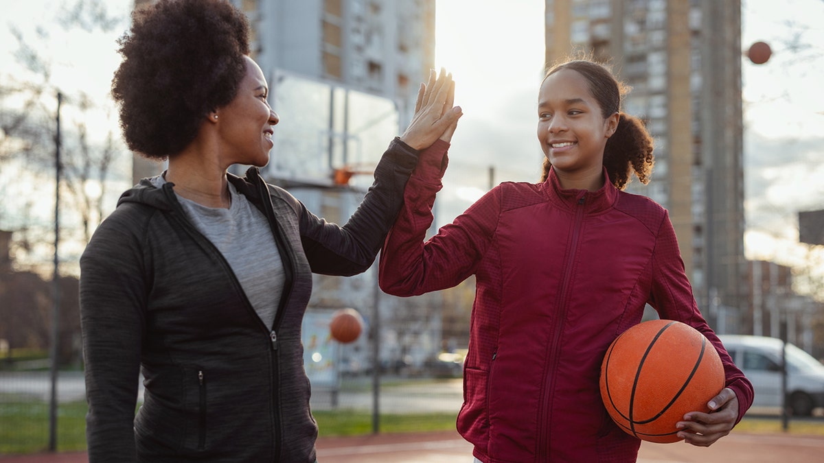 teenage daughter giving high five to her mother while playing basketball