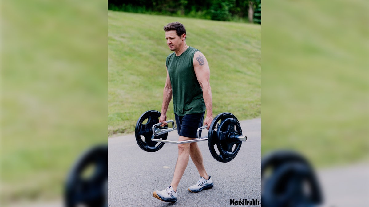 Actor Jeremy Renner wears a green tank top and shorts outside.