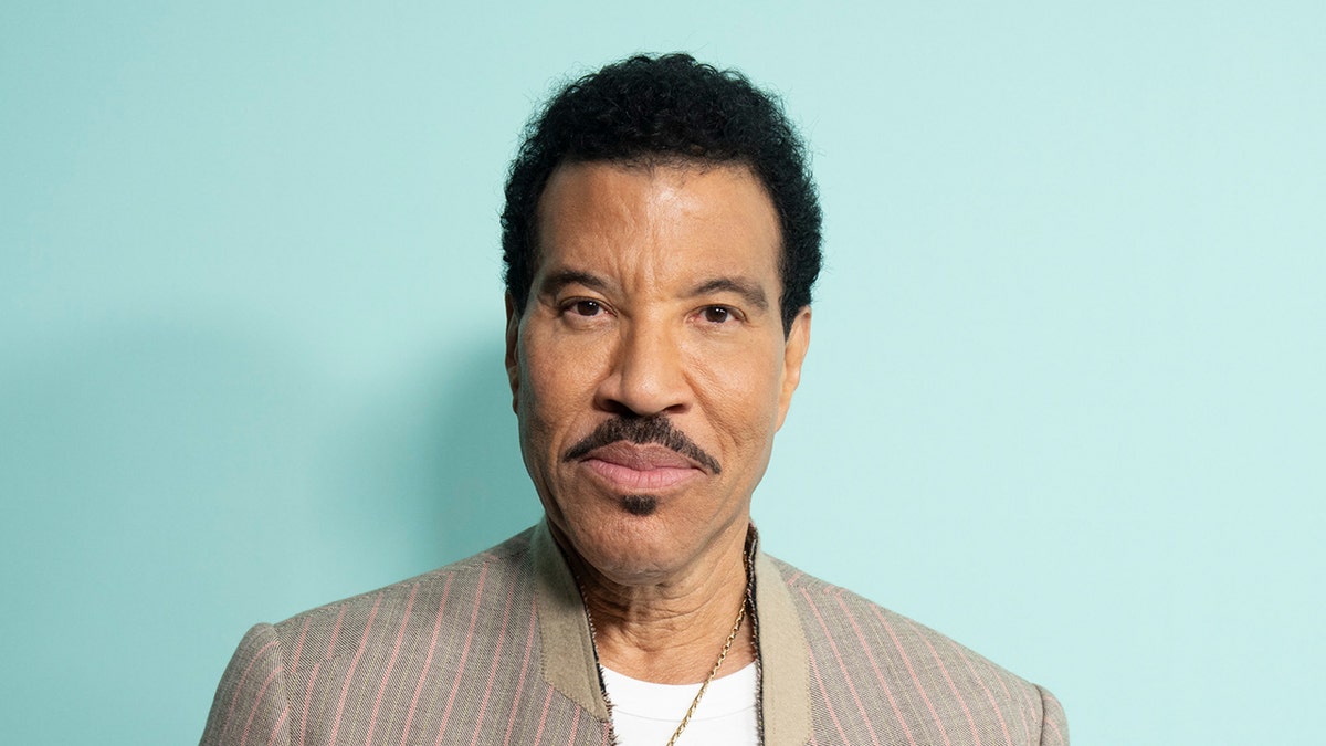 Lionel Richie wears a beige suit with white shirt.