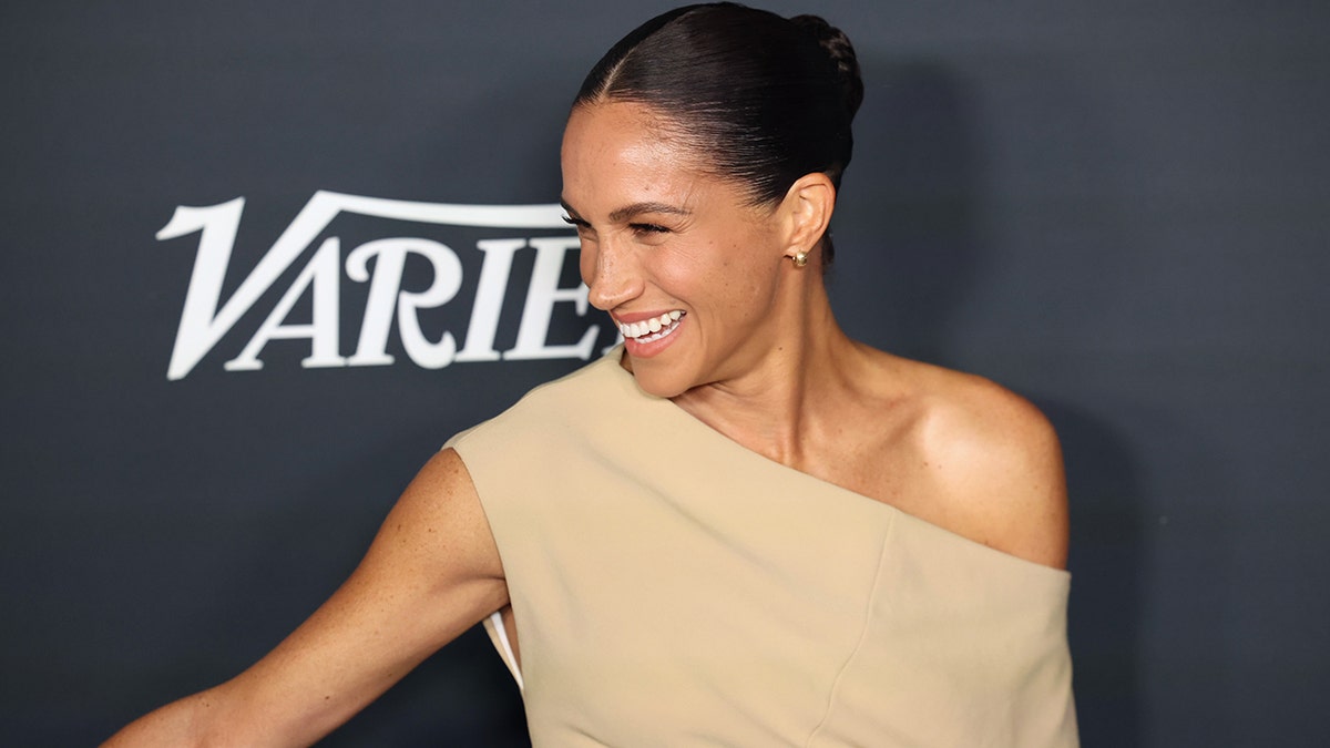 Meghan Markle sonríe con un vestido beige sin hombros