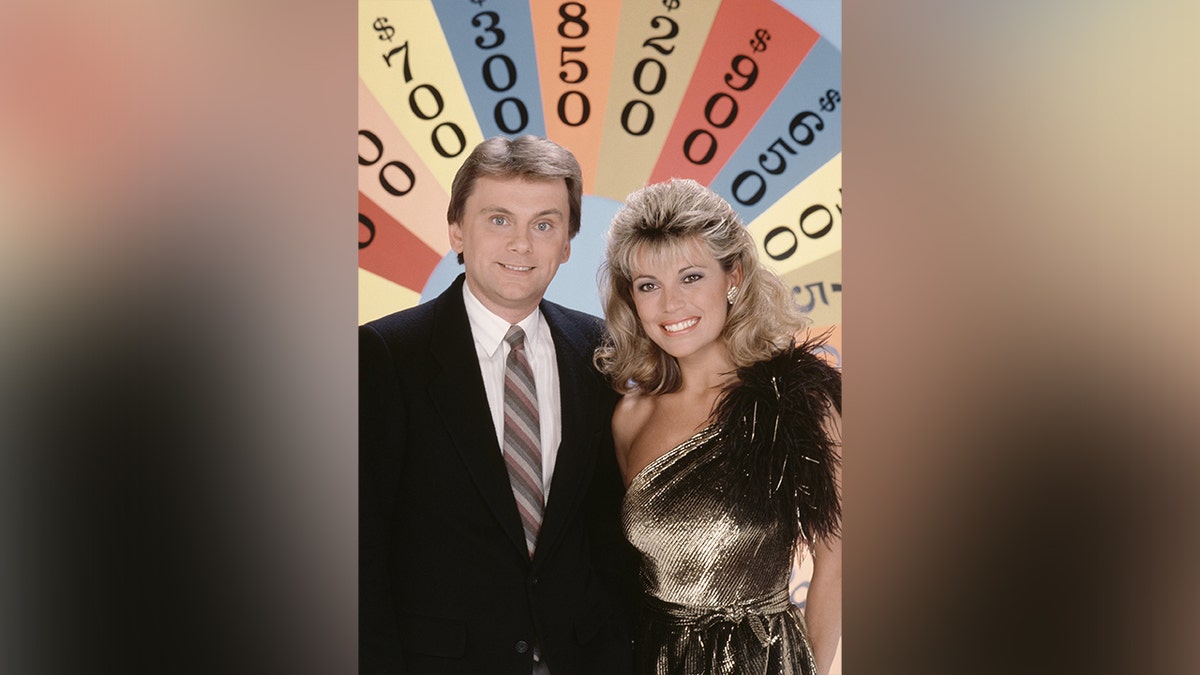 Pat Sajak and Vanna White in front of a vintage board for the game show