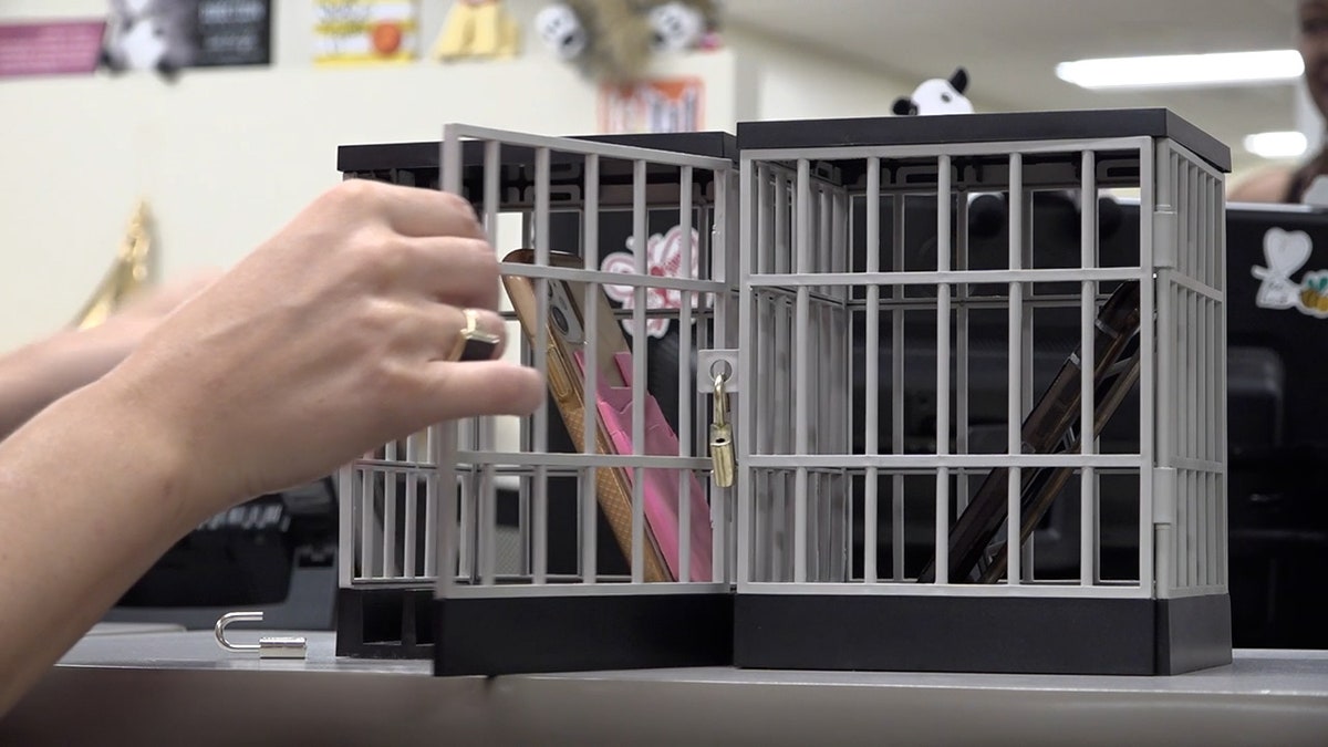 a small cage that looks like a mini jail holds an iphone inside