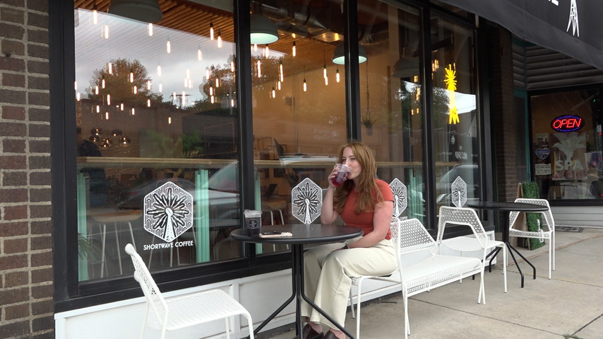 a woman sips a cup of coffee outside a coffee shop sitting at a table