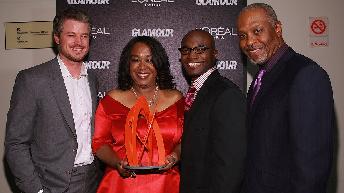Eric Dane in a grey suit stands next to Shonda Rhimes who poses with a red trophy and stands nexxt to Taye Diggs and James Pickens