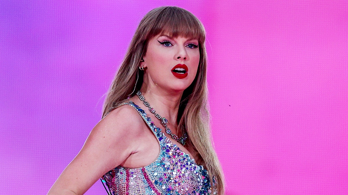 Taylor Swift in a multicolored sparkly bodysuit looks serious as she looks out into the crowd