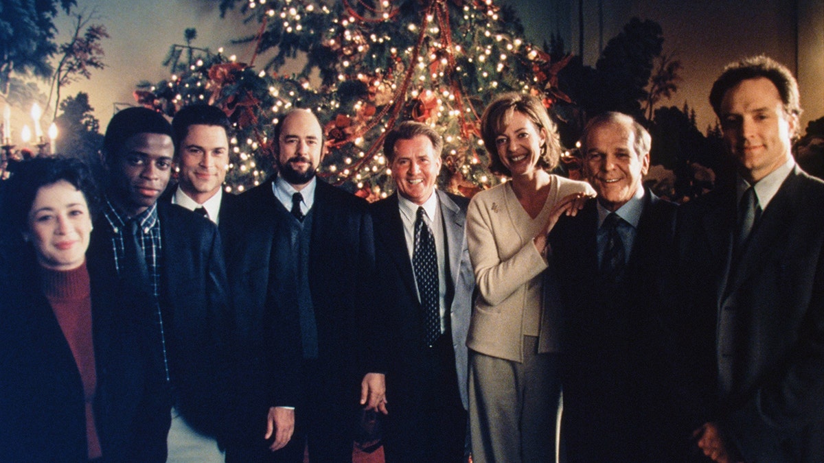 The West Wing cast stands in front of a Christmas tree.