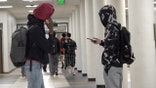 two teenagers talk in a school hallway with one on their phones