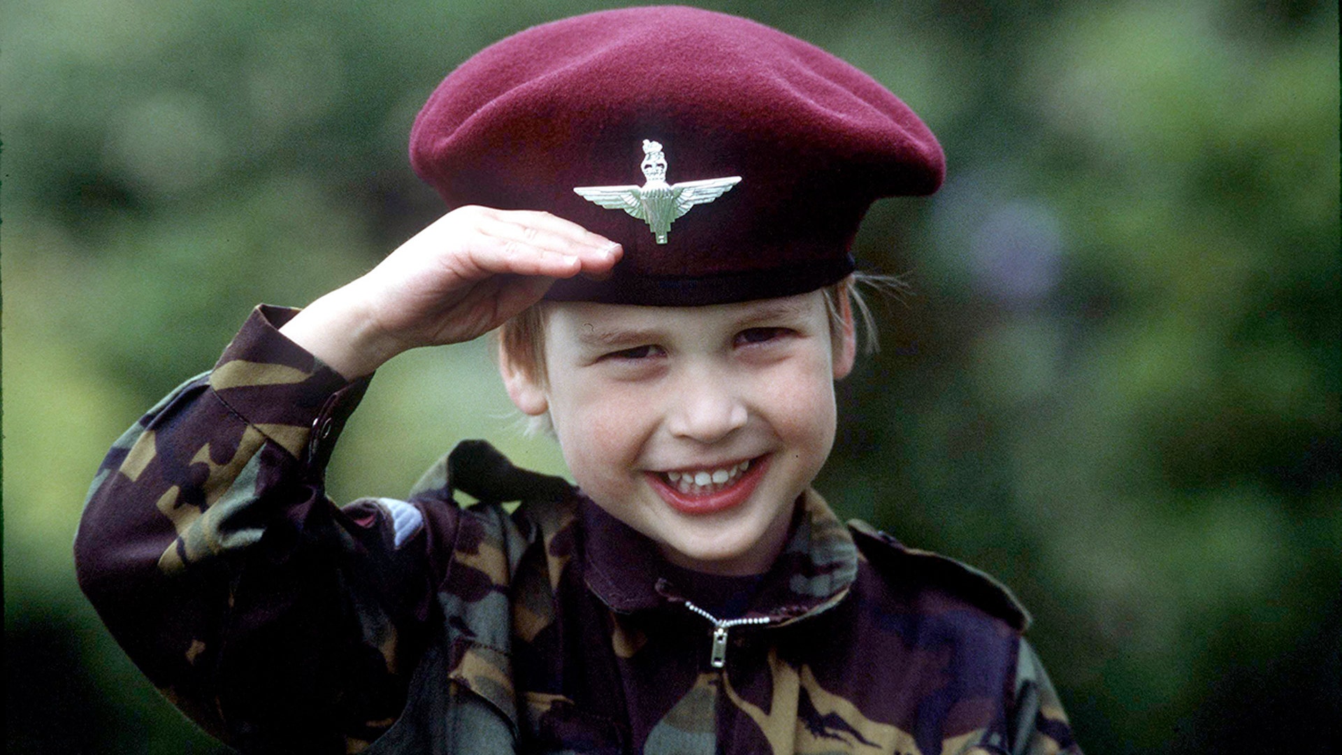 William looks into the camera and salutes while in an army uniform in 1986.