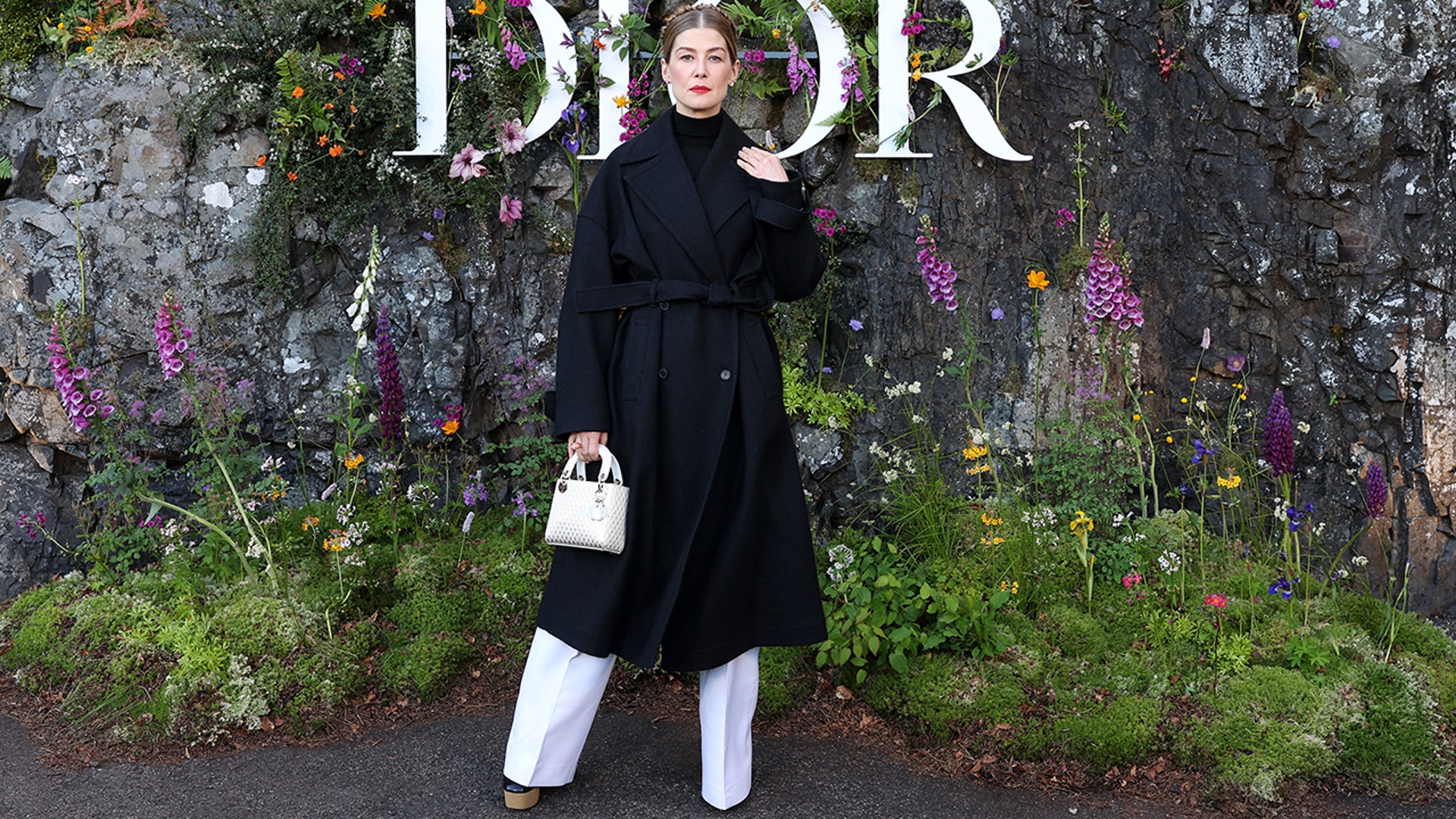 Rosamund Pike wore a long black trench coat and white trousers when attending the Dior fashion show in Scotland.
