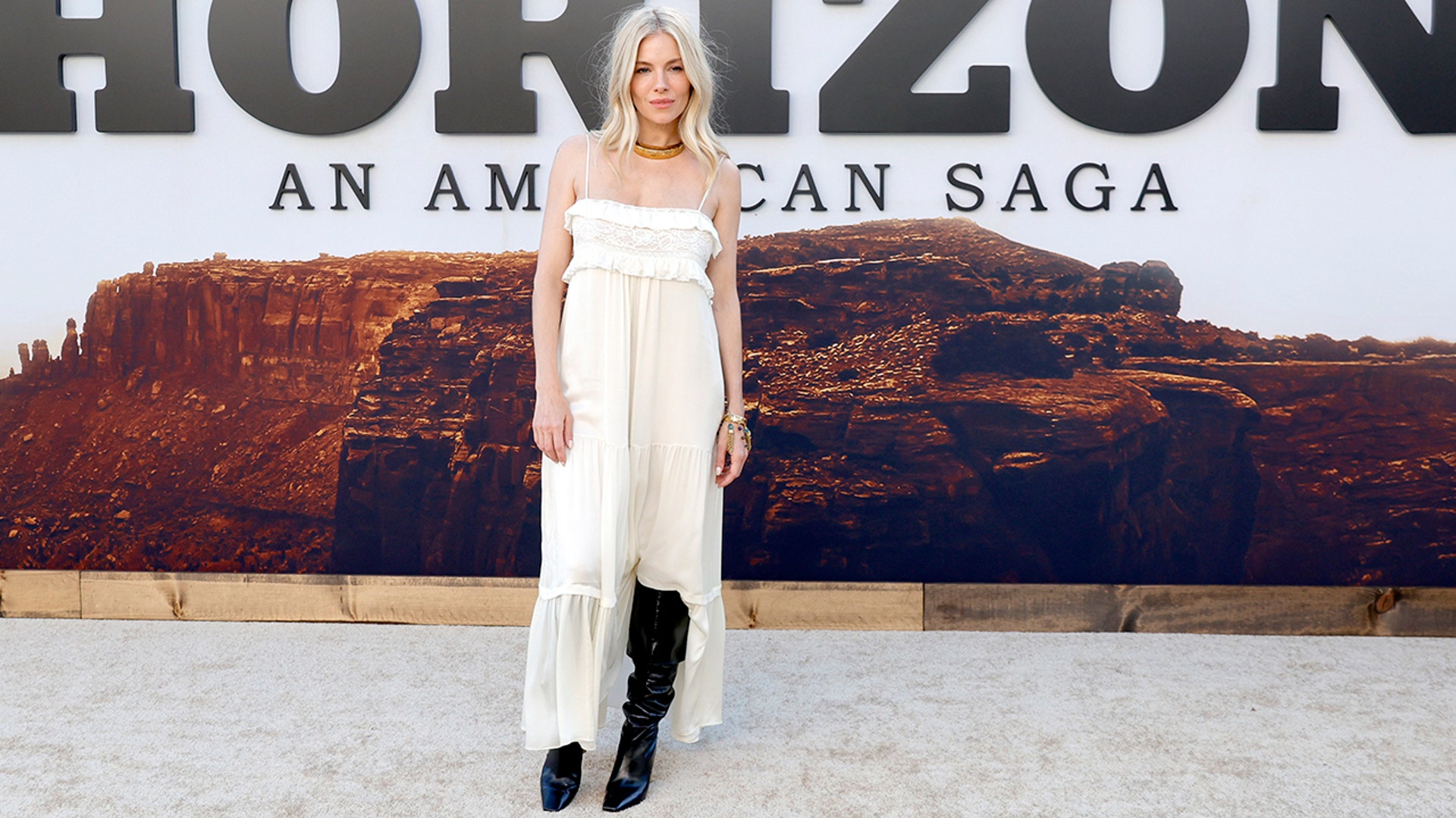 Sienna Miller stunned in a flowy white Chloe dress with lace and ruffles on the red carpet at the premiere of "Horizon: An American Saga - Chapter 1," pairing the dress with knee-high black boots.