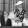 Princess Diana stands back and smiles as she watches her kids, Prince William and Prince Harry, as they look down at the crowd from the balcony.