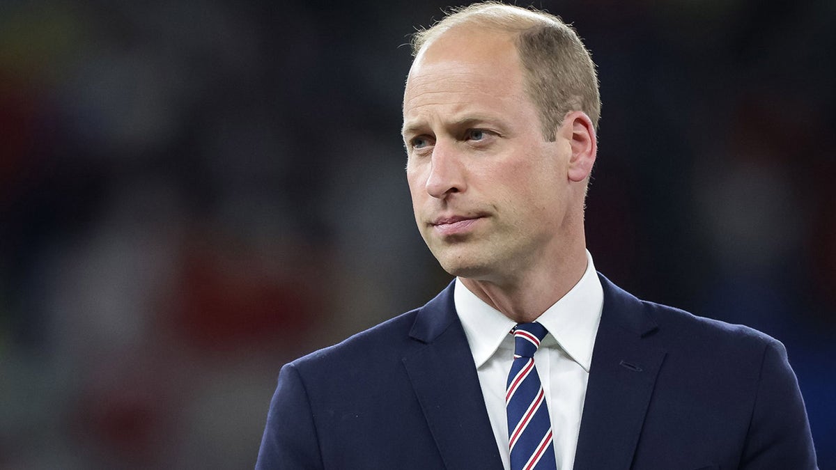 Prince William looking serious in a navy suit with a blue and red and white striped tie.