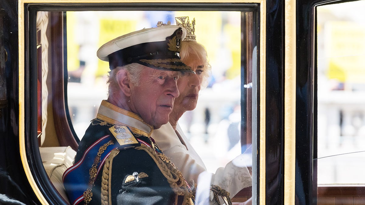 King Charles in a royal uniform sitting next to Queen Camilla in a carriage.