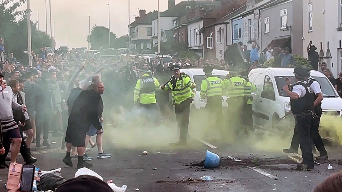 Smoke separates members of the police and the rioting public in Southport, England, right